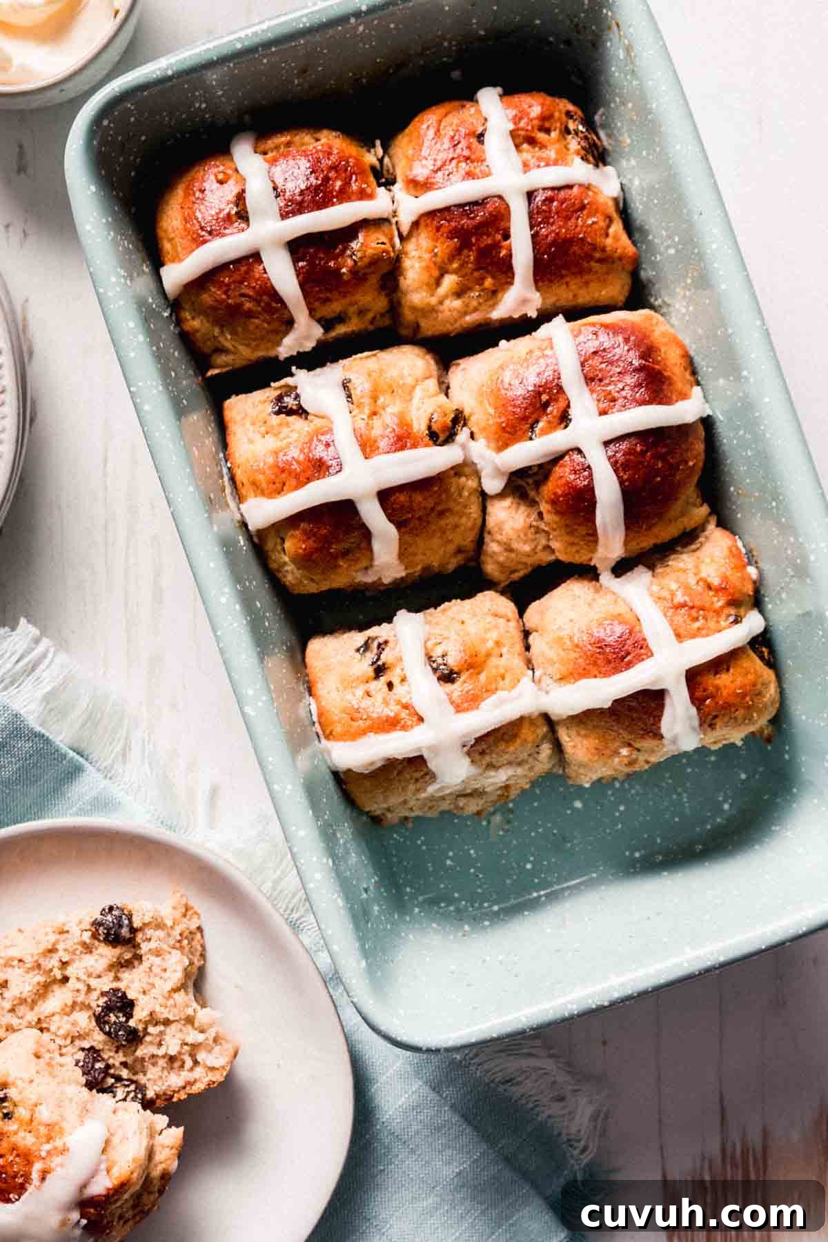 Gluten-free hot cross buns in pan, one split on a plate next to it.