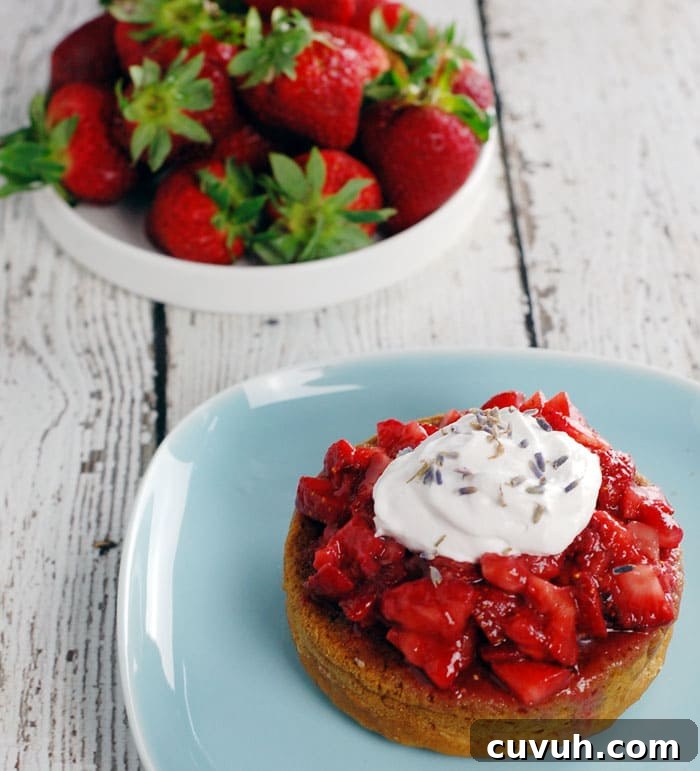Lavender Gin Strawberry Shortcake made with Aquafaba sitting on a pale blue plate and on top of a wooden table painted in white; with a plate full of strawberries in the background