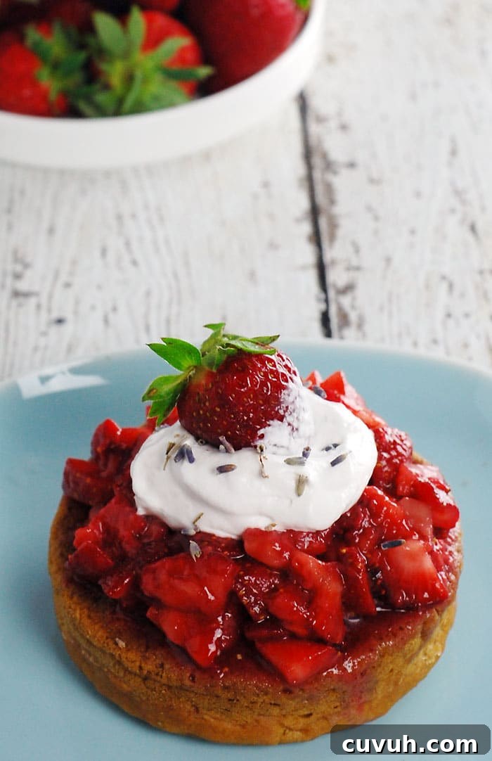 Lavender Gin Strawberry Shortcake made with Aquafaba sitting on a pale blue plate and on top of a wooden table painted in white; with a plate full of strawberries in the background