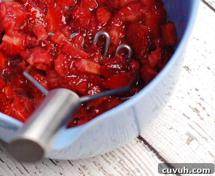 strawberries cut up and mashed in a bowl, sitting on a wooden table painted in white