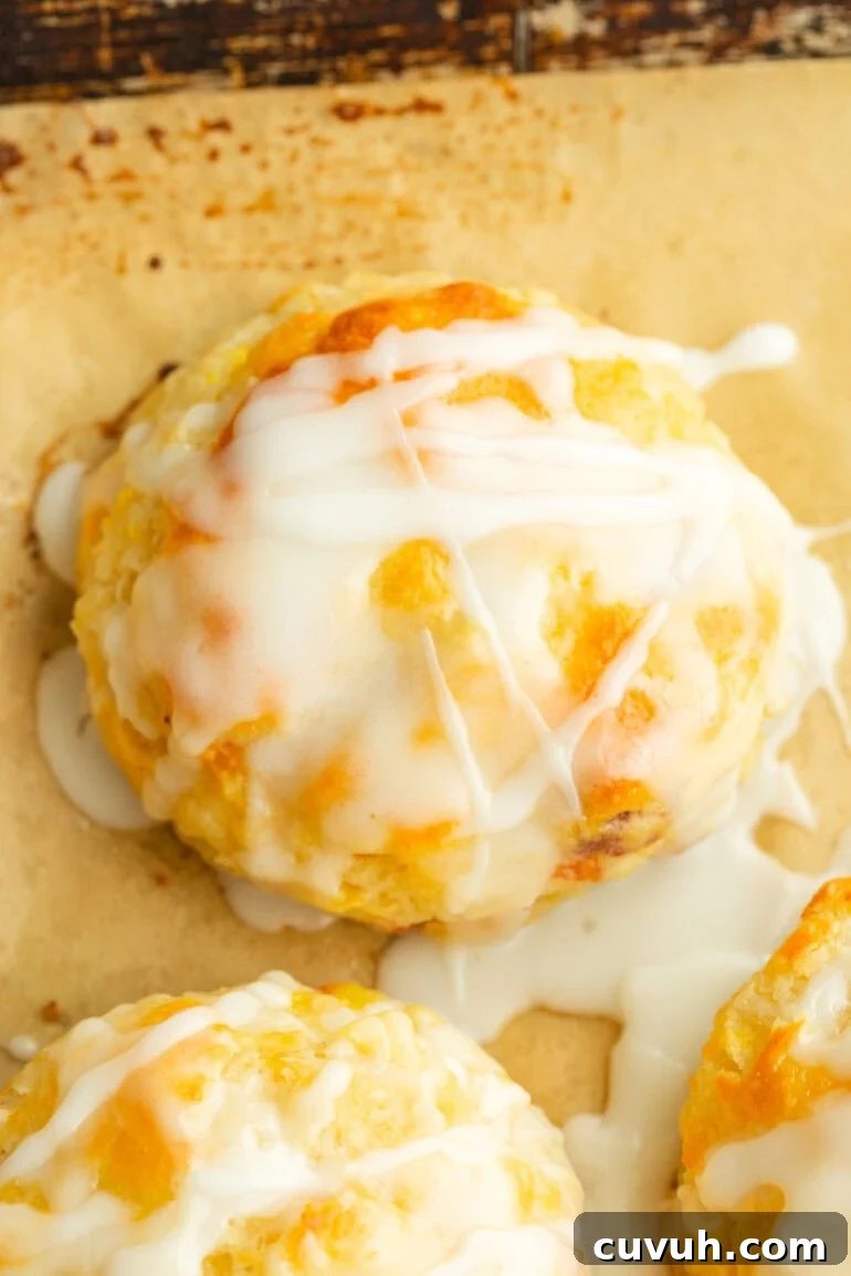 Golden brown biscuit with visible chunks of juicy peach and a smooth glaze dripping down the sides.