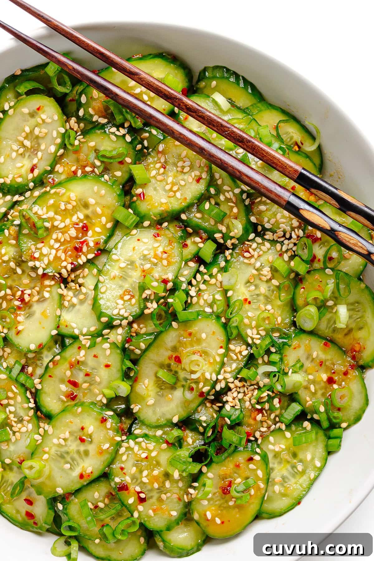 Spicy chili crisp cucumber salad in white bowl with chopsticks.