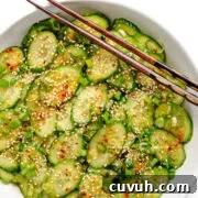 Spicy chili crisp cucumber salad in a white bowl with chopsticks set across a corner.
