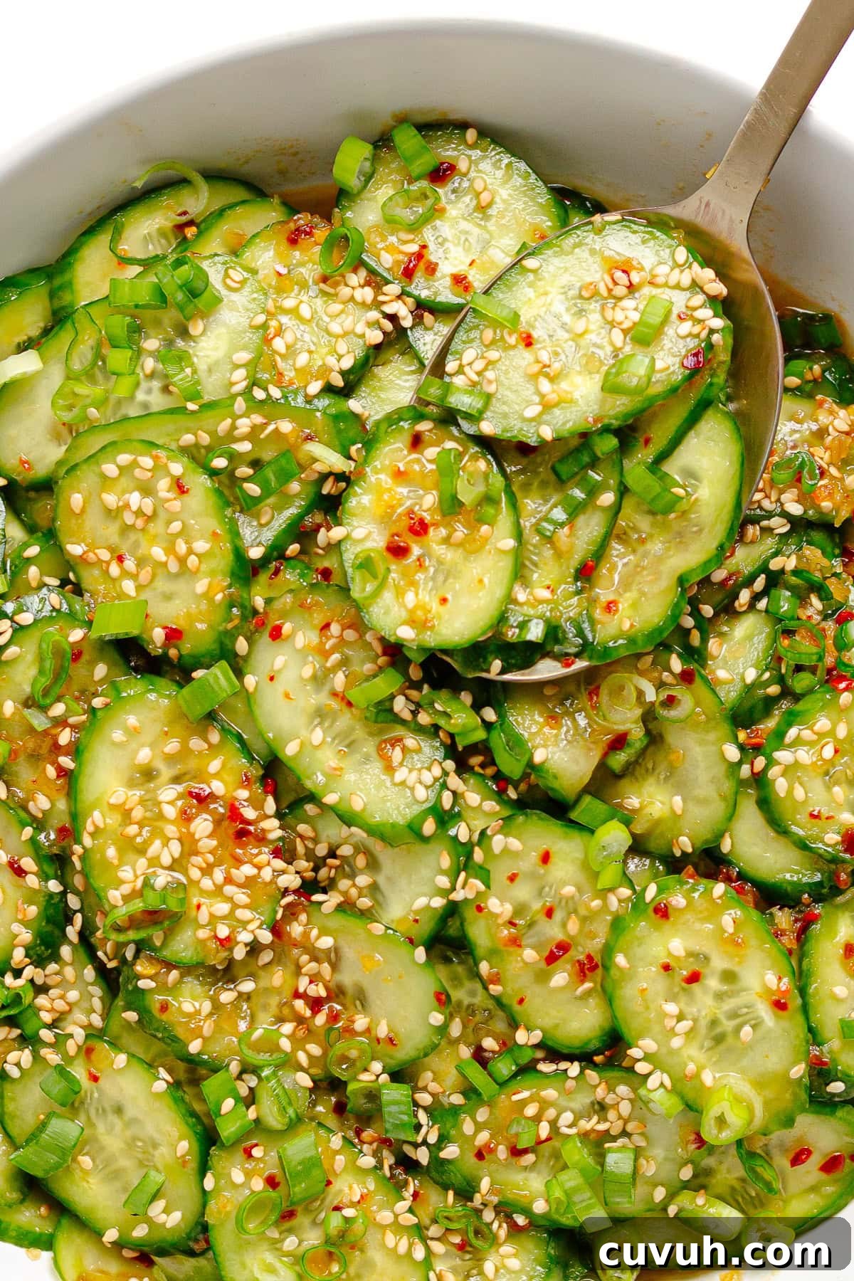 Serving spoon lifting some chili crisp cucumber salad from bowl.