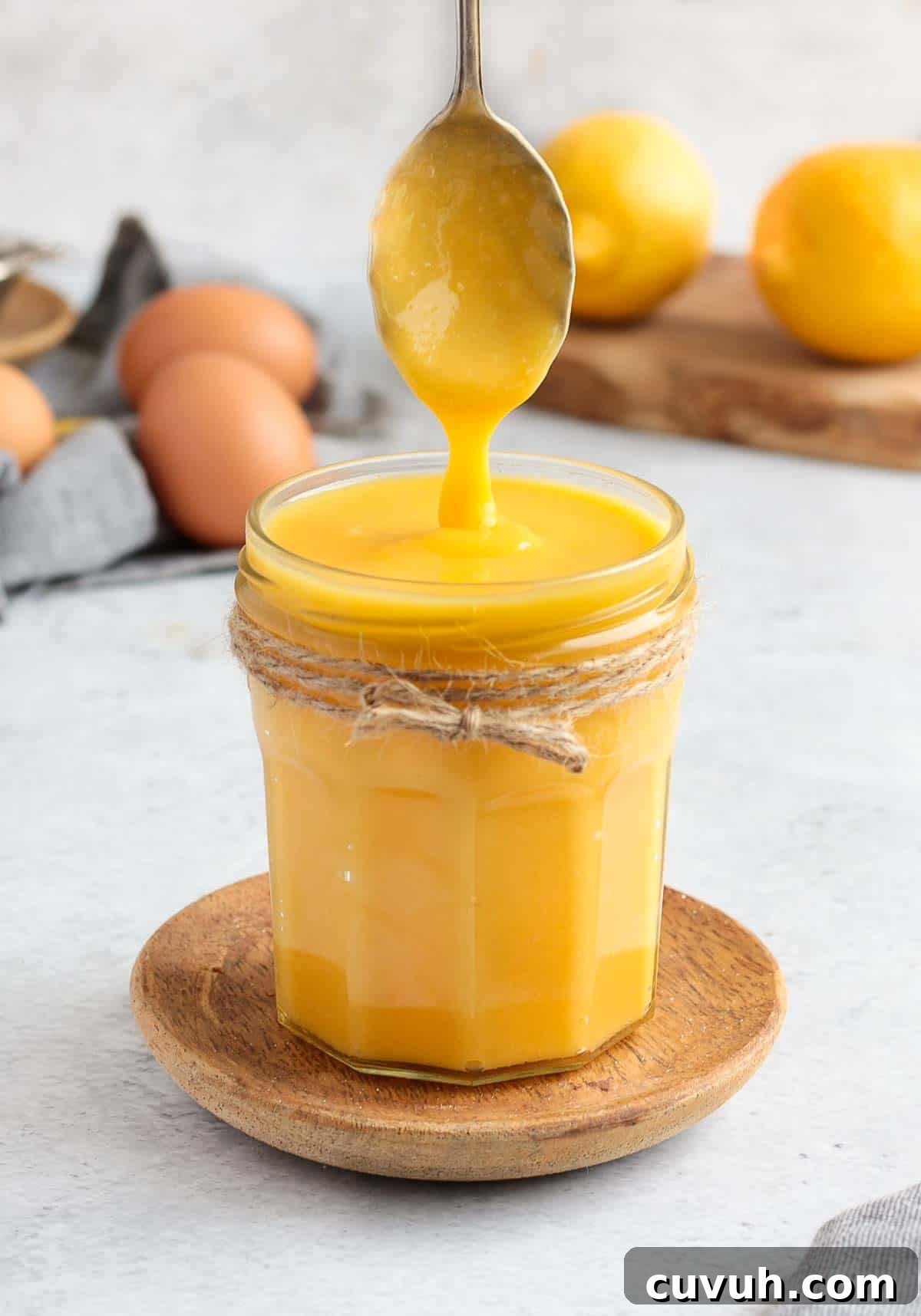 Curd dripping from a metal spoon into the glass jar.