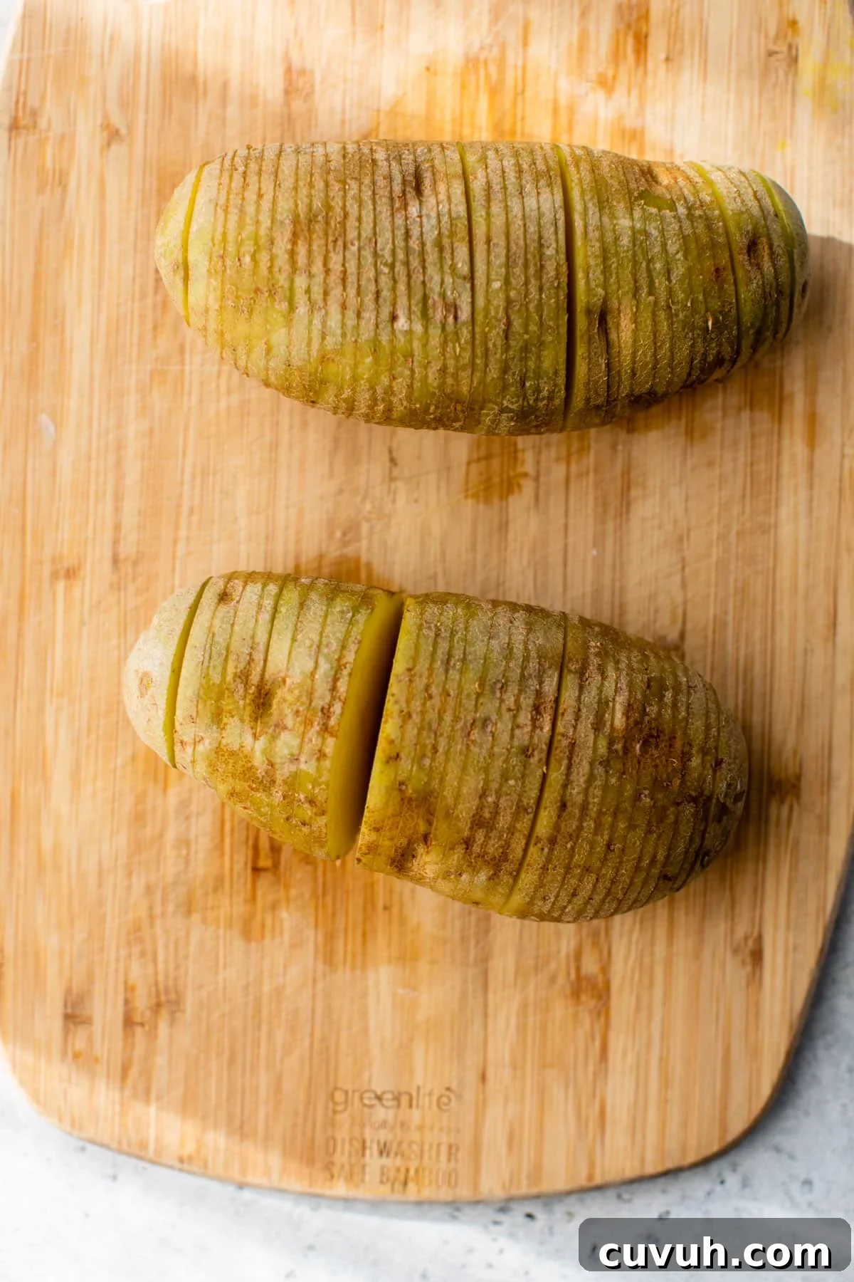 2 potatoes with slices though them on a cutting board