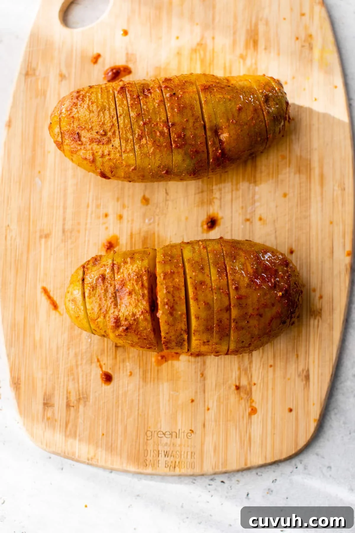 2 potatoes with slices through them and the buttery mix poured over top on a cutting board