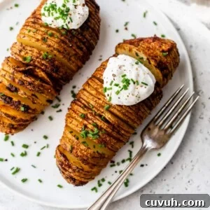 2 hasselback potatoes with sour cream and chives on top on a plate with a fork