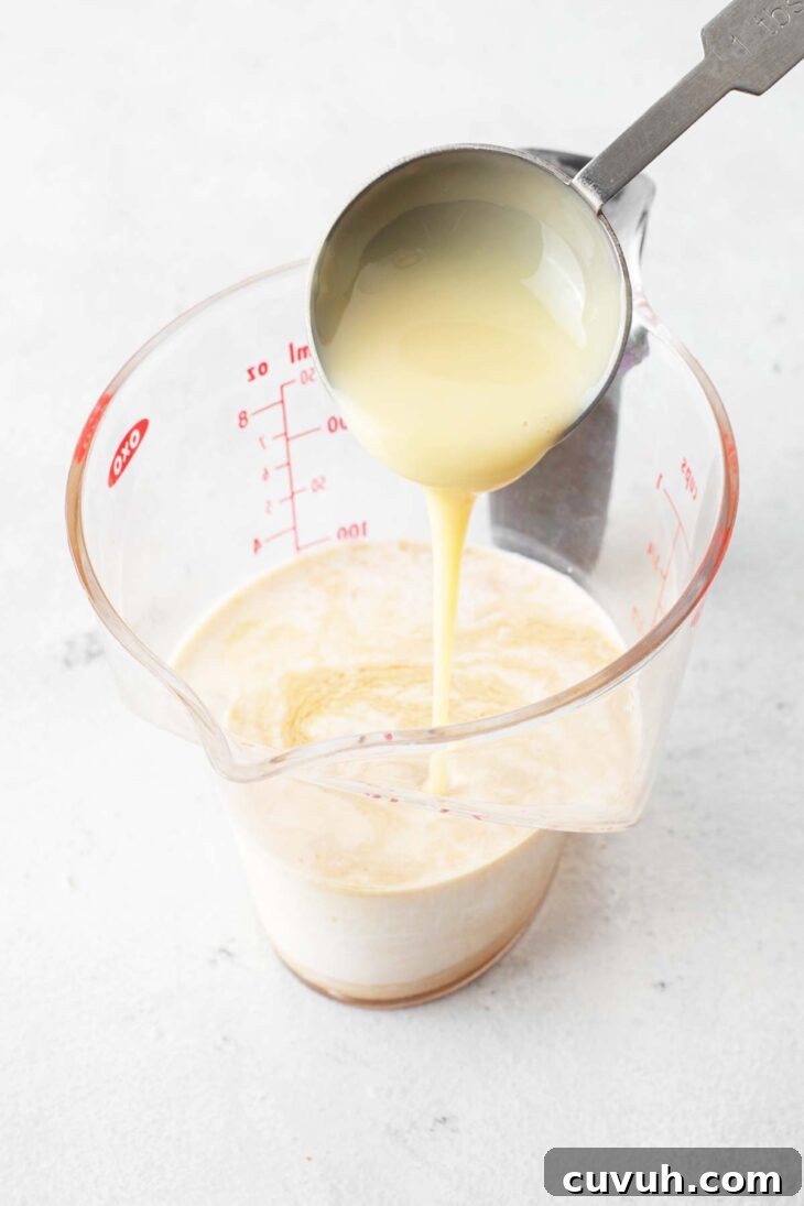 Pouring sweetened condensed milk into a measuring cup with half & half.
