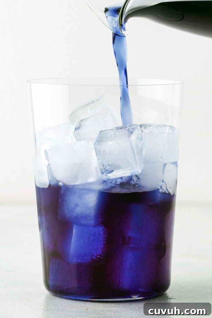 Pouring blue tea into a cup with ice.