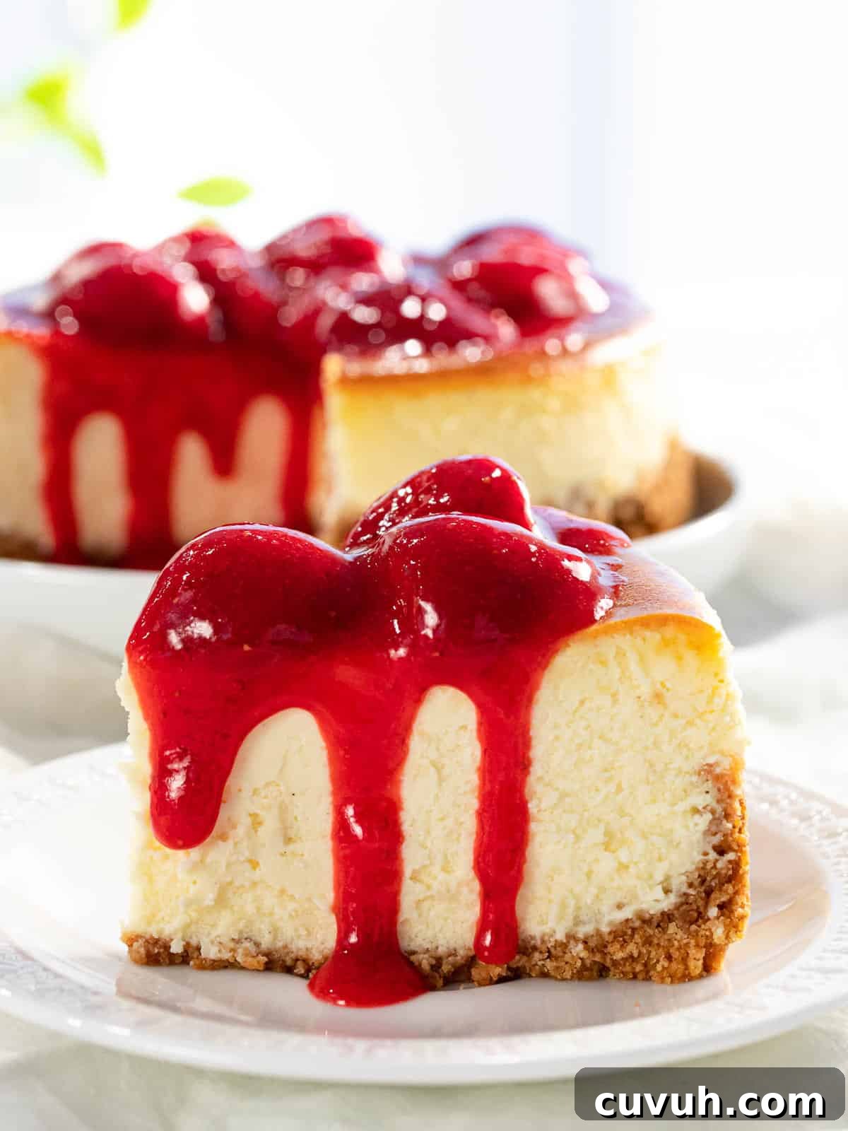 Decadent Strawberry Cheesecake Recipe with Fresh Berry Topping 3 A slice of strawberry cheesecake with strawberry sauce dripping down the sides.