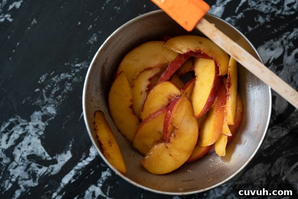 Keto Peach 'n' Cream Shortcake Recipe for Low-Carb Desserts 3 Sliced peaches macerating in a metal bowl over a black marble surface with a spatula on the side