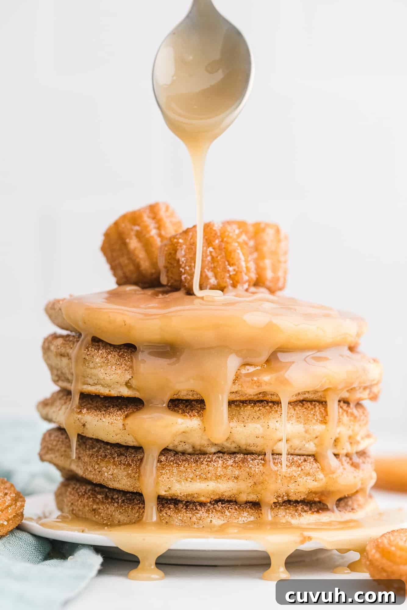 A stack of pancakes topped with churros, being drizzled with syrup.