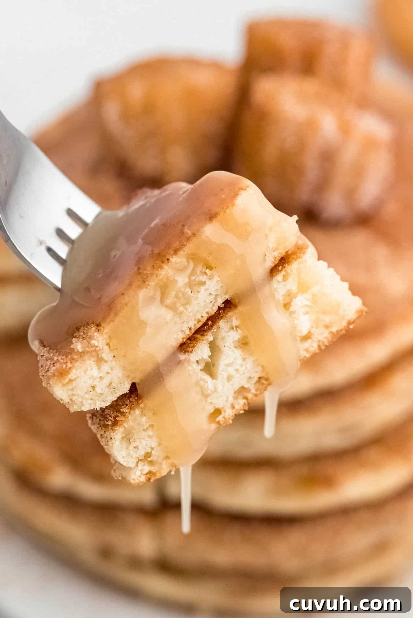A fork holds a caramel-drizzled piece of pancake, with a stack of pancakes and cinnamon sugar-coated churros in the background.