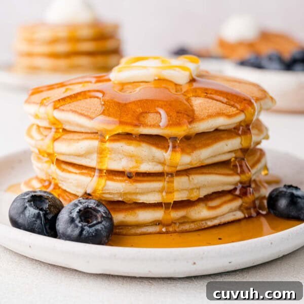 A stack of pancakes topped with butter and syrup on a plate, with blueberries beside them.