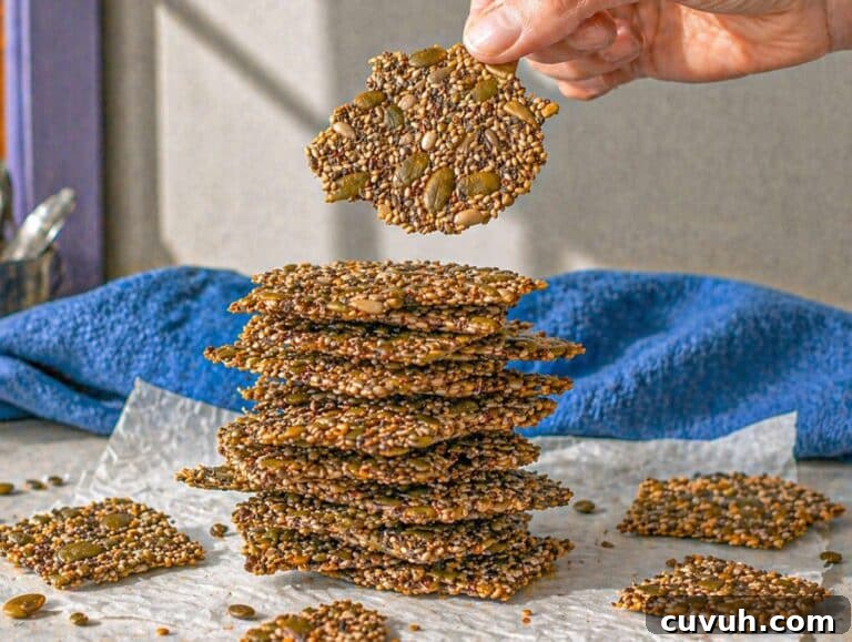 Crispy Seed Crackers: Flour-Free Savory Snack Recipe 13 Step 4 Hand holding a thin seed cracker above a stack of crispy crackers on marble.