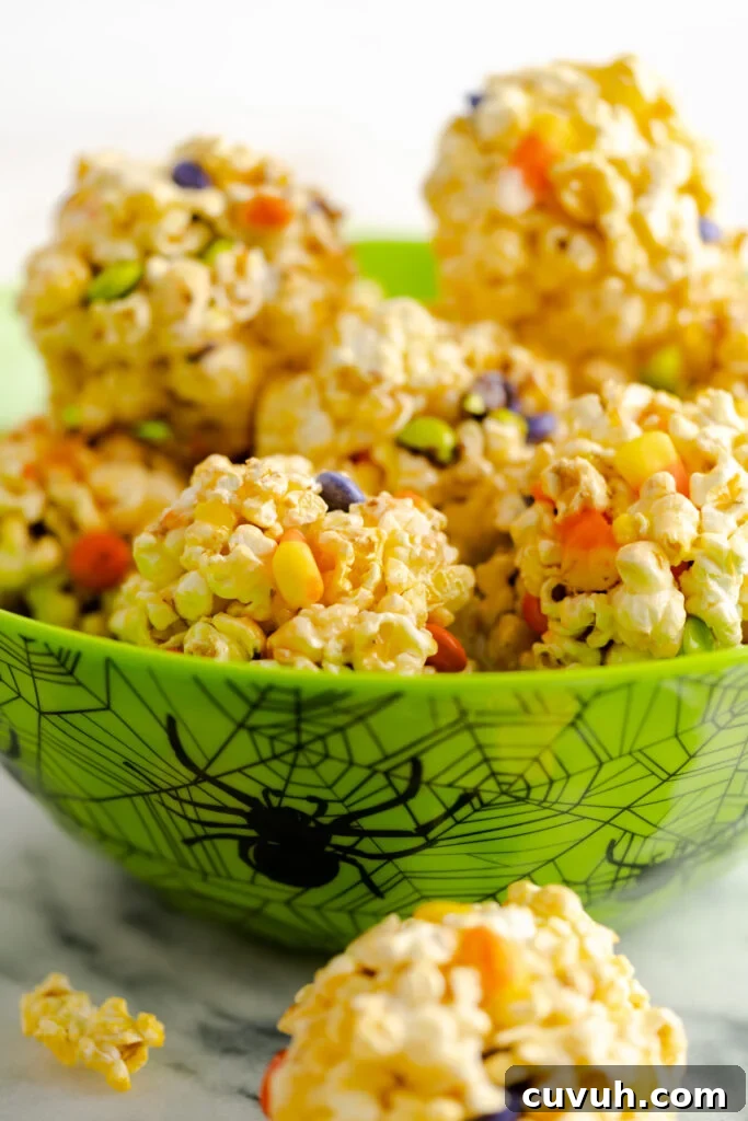 Halloween popcorn balls in green bowl decorated with spiders and webs.