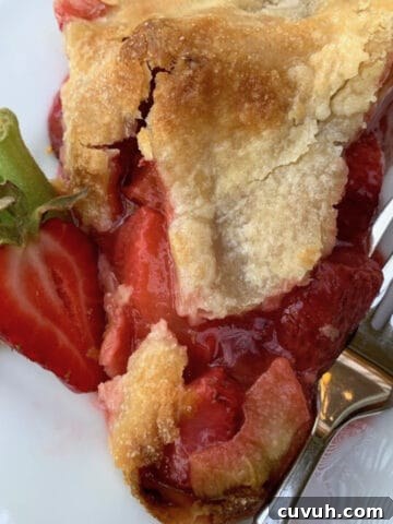 A slice of strawberry rhubarb pie on a plate with a fork on the side.