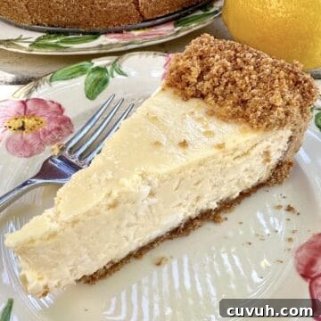 A slice of vanilla cheesecake on a plate with the rest of the cake and a lemon in the background.
