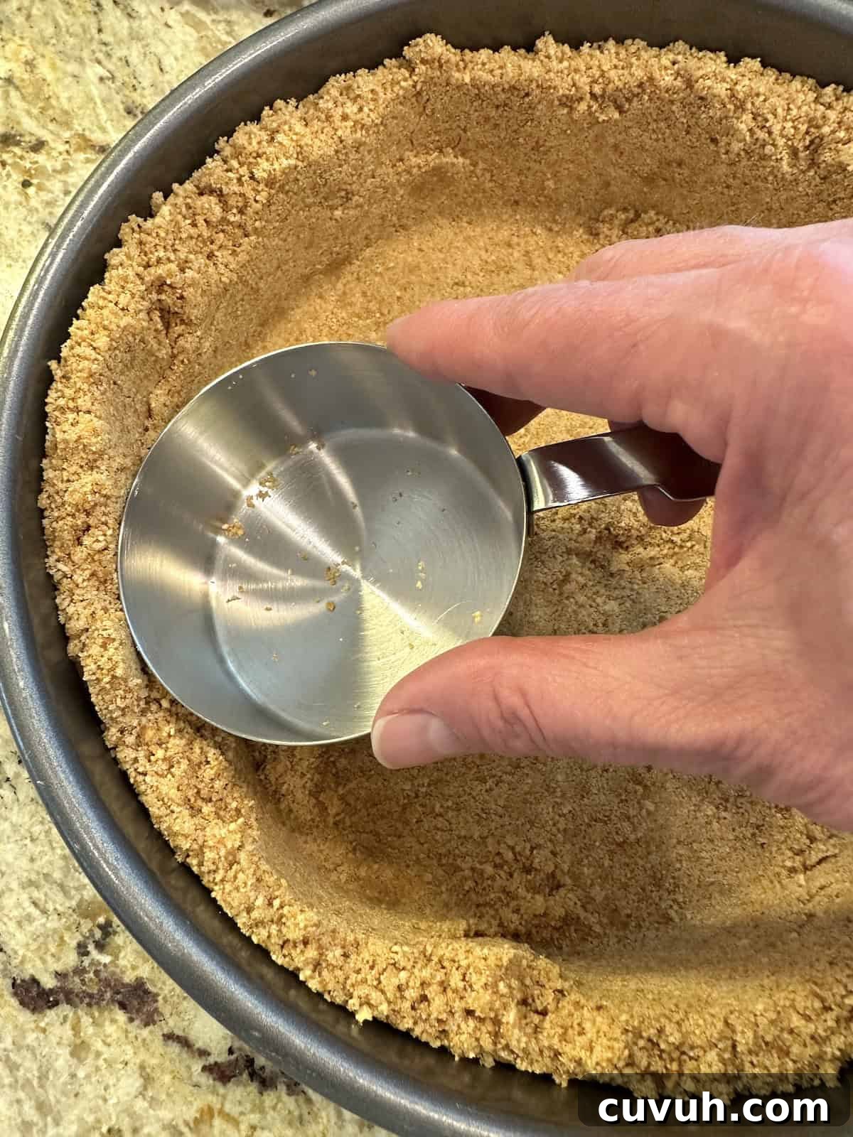 An empty measuring cup used to flatten graham cracker crust ingredients in a baking pan.