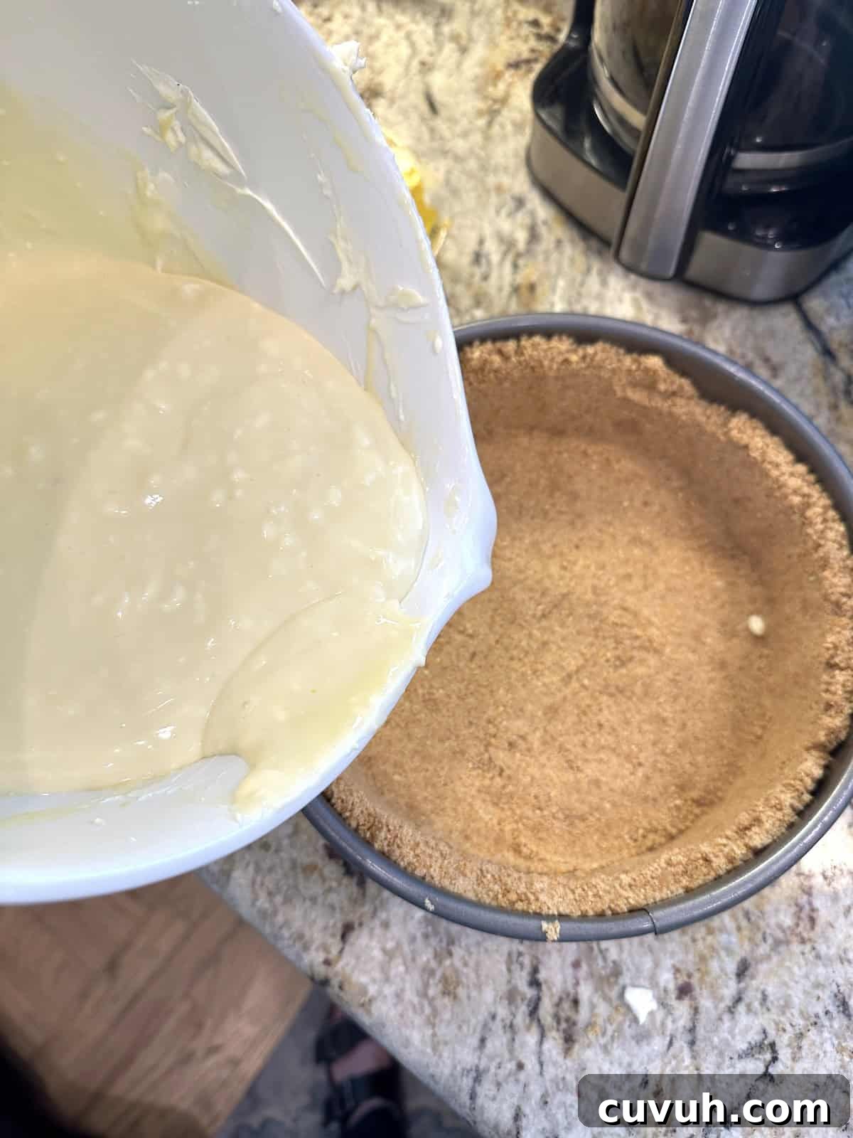 A mixing bowl full of cheesecake filling over a graham cracker crust in a cake pan.