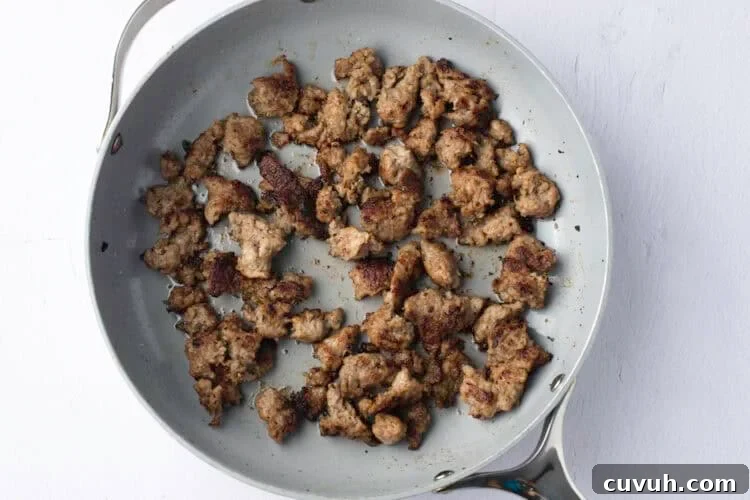 Overhead view of browned and crumbled sausage in a large skillet.