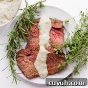 A few slices of herb mustard crusted roast beef on a white plate with creamy herb sauce drizzled over top.