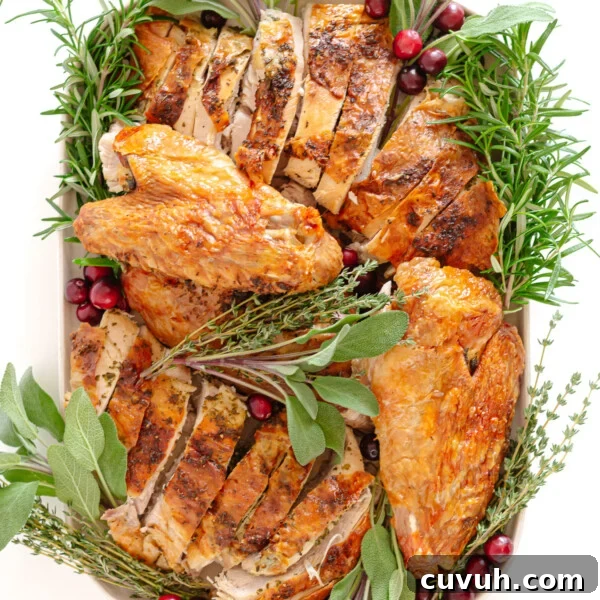 Carved dry brined spatchcock turkey with herb butter on a platter garnished with herbs and cranberries.