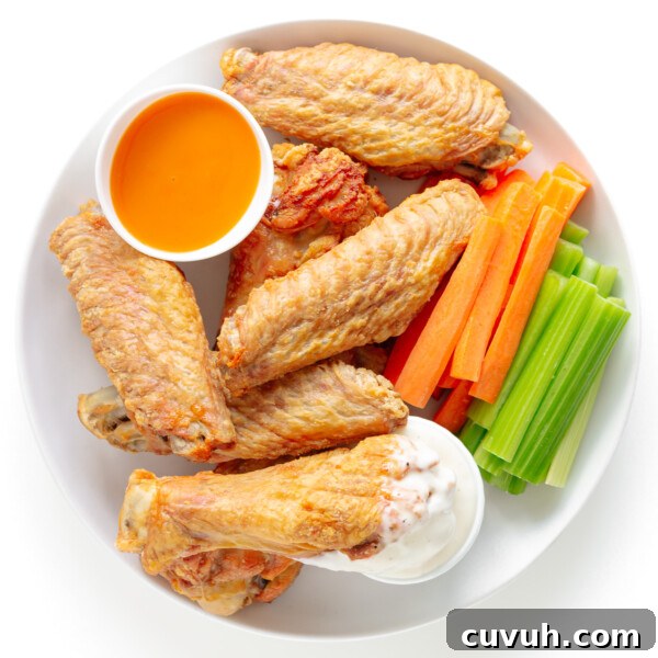 Crispy baked turkey wings on a white plate served with two dipping sauces, carrot and celery sticks.