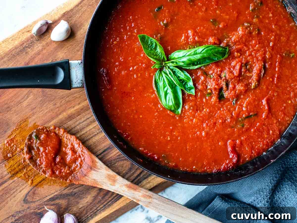 Authentic San Marzano Tomato Sauce Recipe for Homemade Pasta 10 Overhead view of tomato sauce in a black skillet with basil sprig in the middle of the sauce.