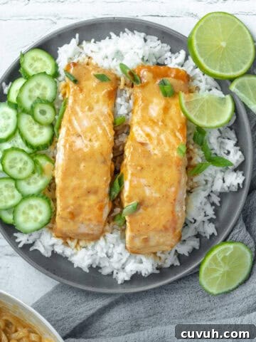 Thai red curry salmon on a bed of rice with limes and cucumbers.