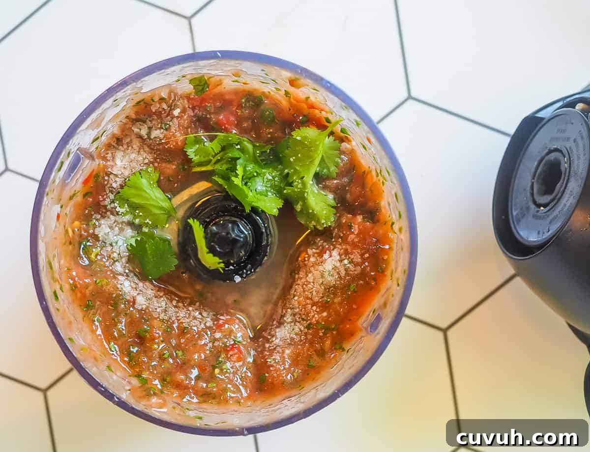 Fresh Garden Salsa Ready in 5 Minutes 5 A blender with salsa in it on a white tiled background.