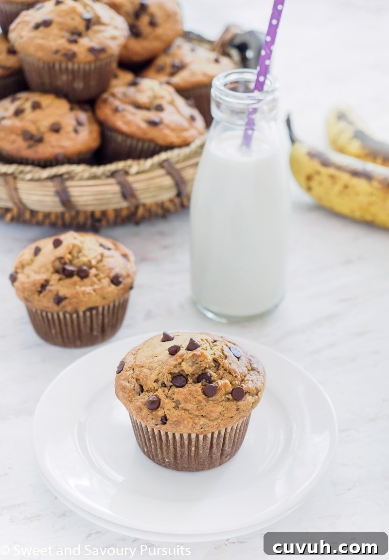 A basket of Banana Oatmeal Chocolate Chip Muffins with one muffin on small dish served with milk.