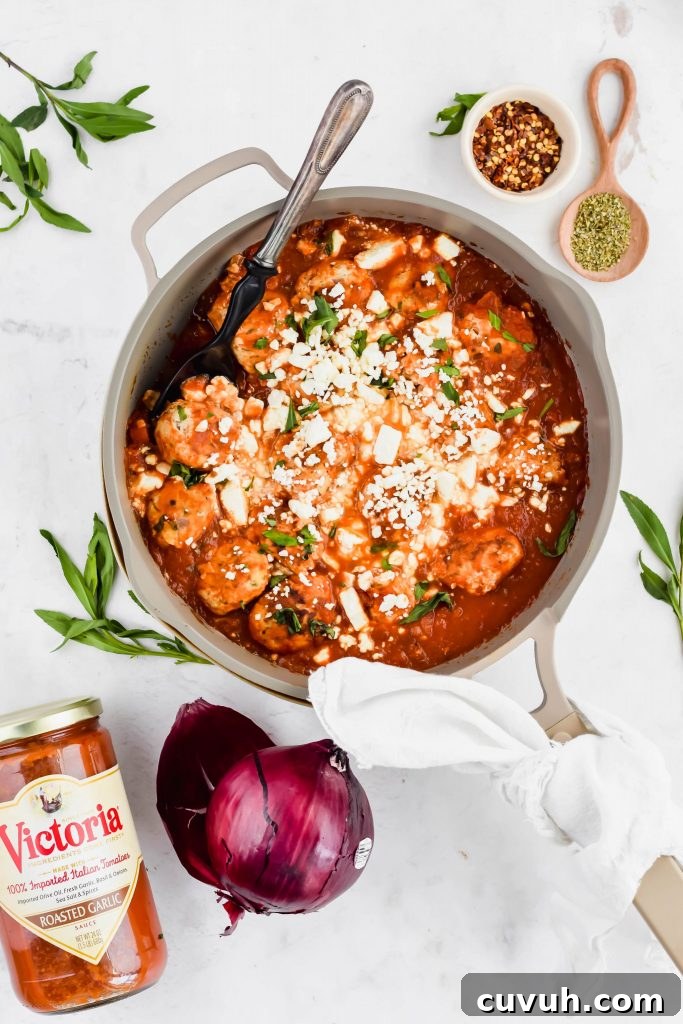 Turkey Feta Meatballs in a gray skillet with a serving spoon surrounded by spices, red onion, and a jar of tomato sauce.