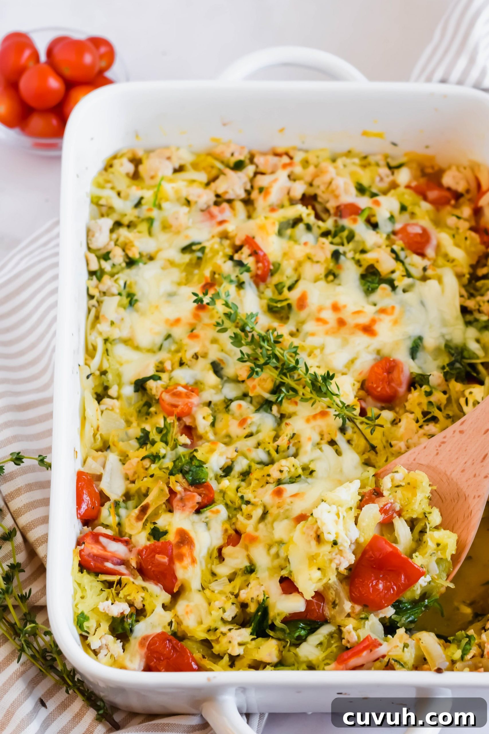 Large white baking dish with spaghetti squash feta cheese casserole recipe with wooden spoon topped with fresh thyme sprig in dish.