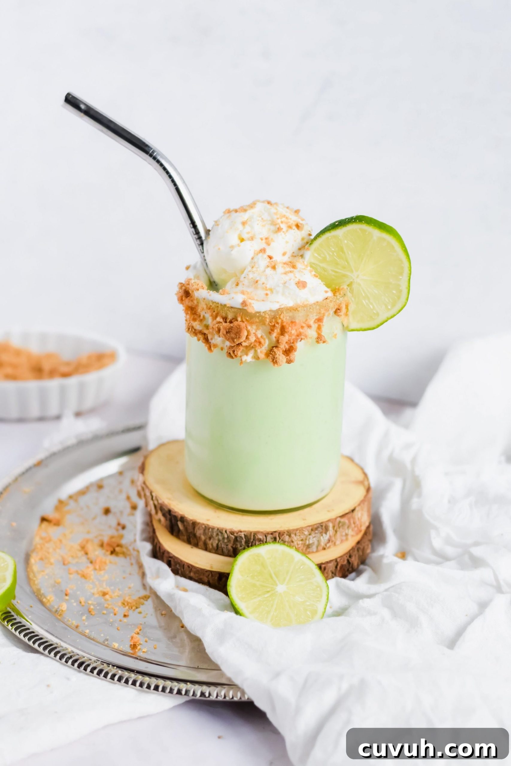 Key Lime Pie Milkshake topped with Cool Whip, crumbled graham cracker and a slice of lime with a metal straw.