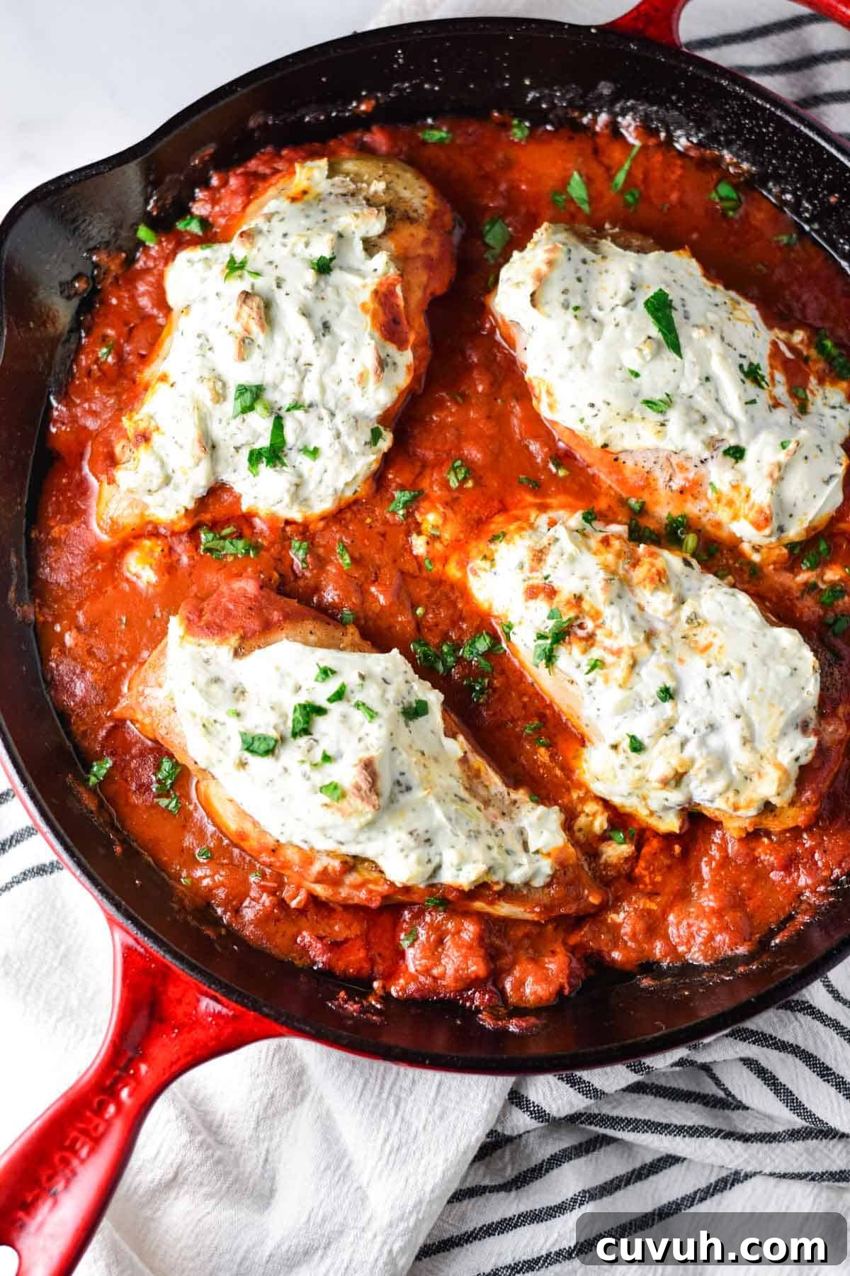 A large cast iron pan with 4 chicken breasts topped with a creamy ricotta mix. 