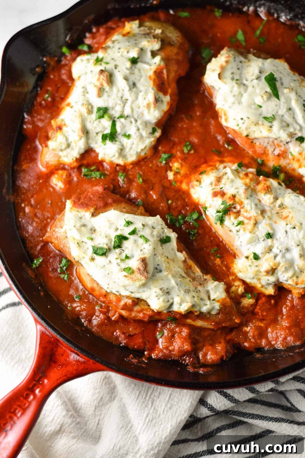 A red pan with chicken breasts topped with ricotta cheese and parsley.