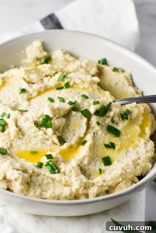 A roasted mashed cauliflower in a bowl with a spoon on a white table