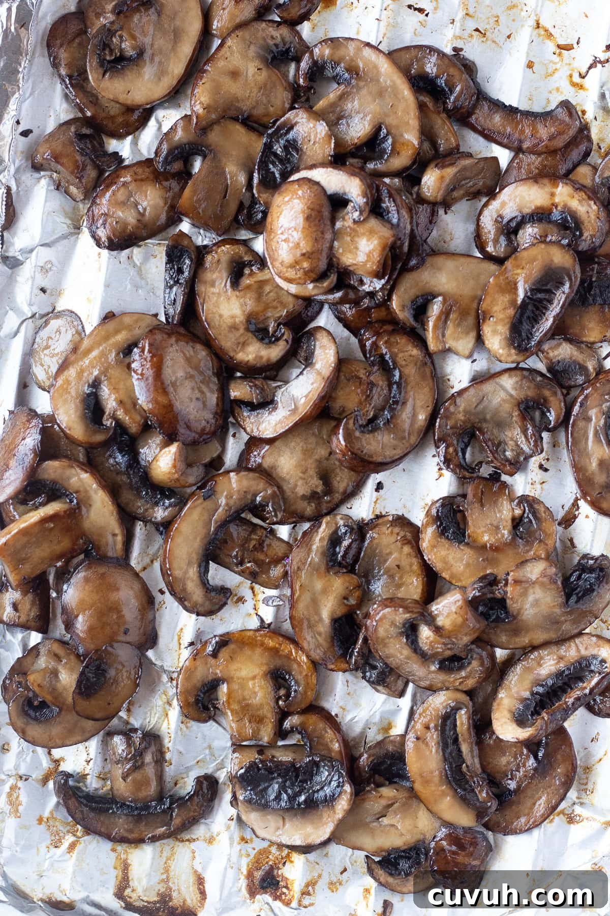 Grilled Foil-Wrapped Mushrooms with Garlic and Herbs 2 A close-up image of sliced, grilled mushrooms spread out on a piece of crumpled aluminum foil. The mushrooms are a mix of dark and light brown hues, with a slightly glossy texture, indicating they are cooked.