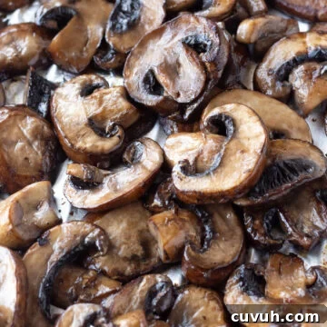 Grilled Foil-Wrapped Mushrooms with Garlic and Herbs 12 A close-up image showing a pile of freshly grilled mushrooms in foil, evenly browned and glistening with oil. The slices are of varying sizes and are spread out, showcasing their textured surfaces and gills.