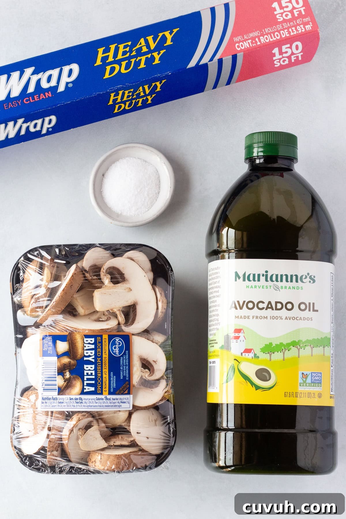 Grilled Foil-Wrapped Mushrooms with Garlic and Herbs 3 Image showcasing a package of baby bella mushrooms, a large bottle of avocado oil, a container of kosher salt, and a roll of heavy-duty aluminum foil on a light-colored surface.