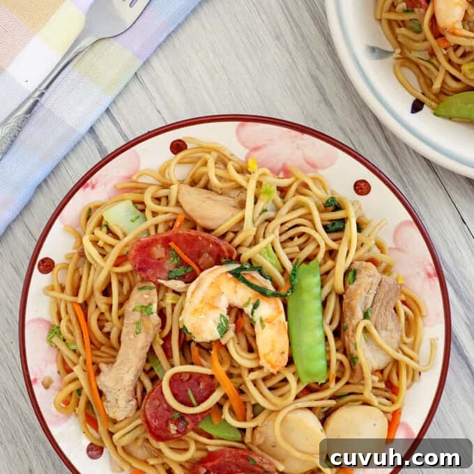 Filipino pancit canton guisado with shrimp, sausage, and veggies on a plate