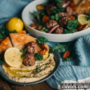 lamb meatballs on a plate with hummus and pita, lemon wedges and herbs for garnish