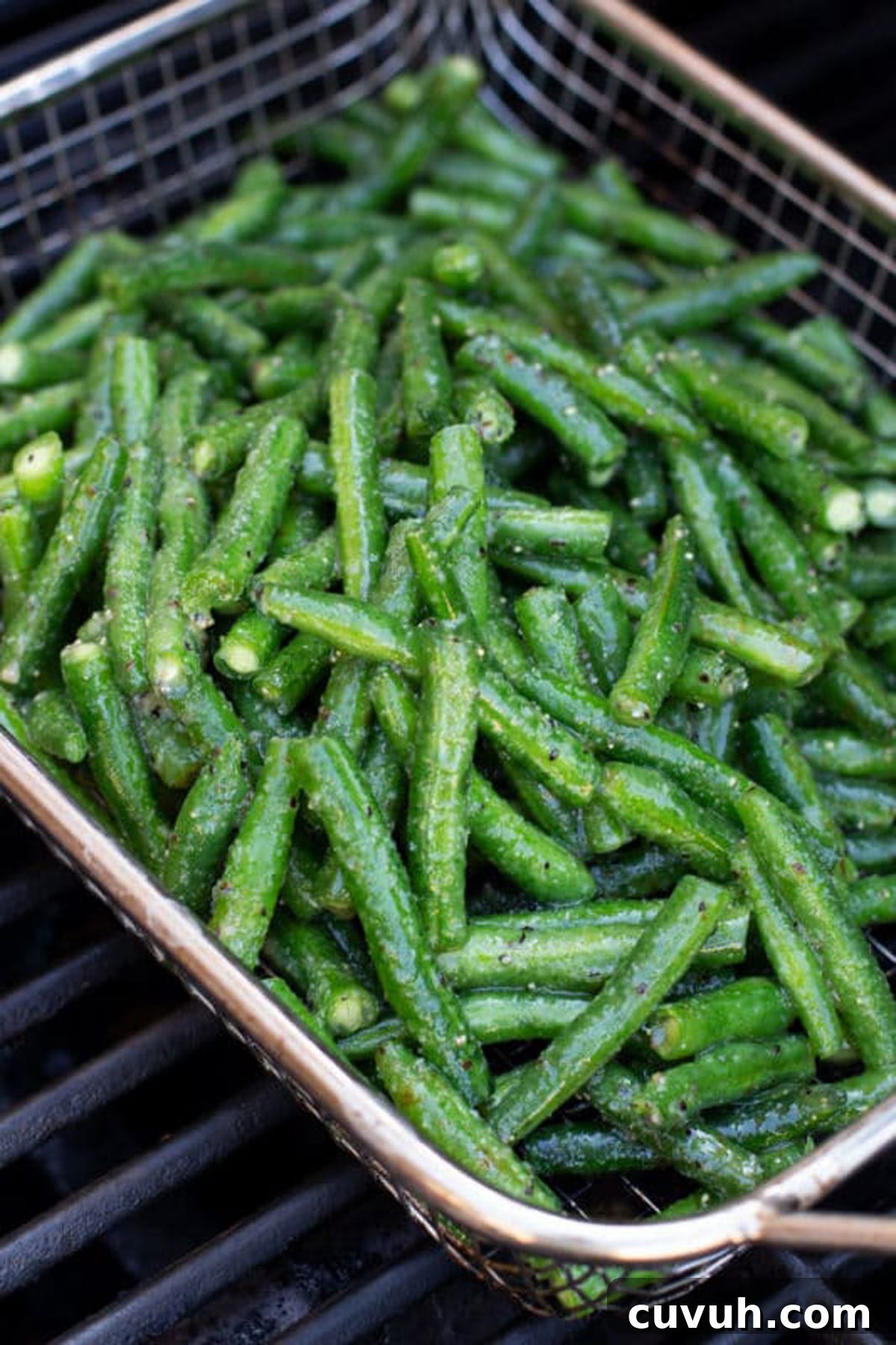Fresh green beans being grilled in a basket on a grill.