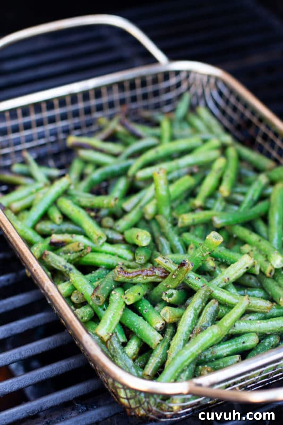 Fresh green beans in a grilling basket on a grill.