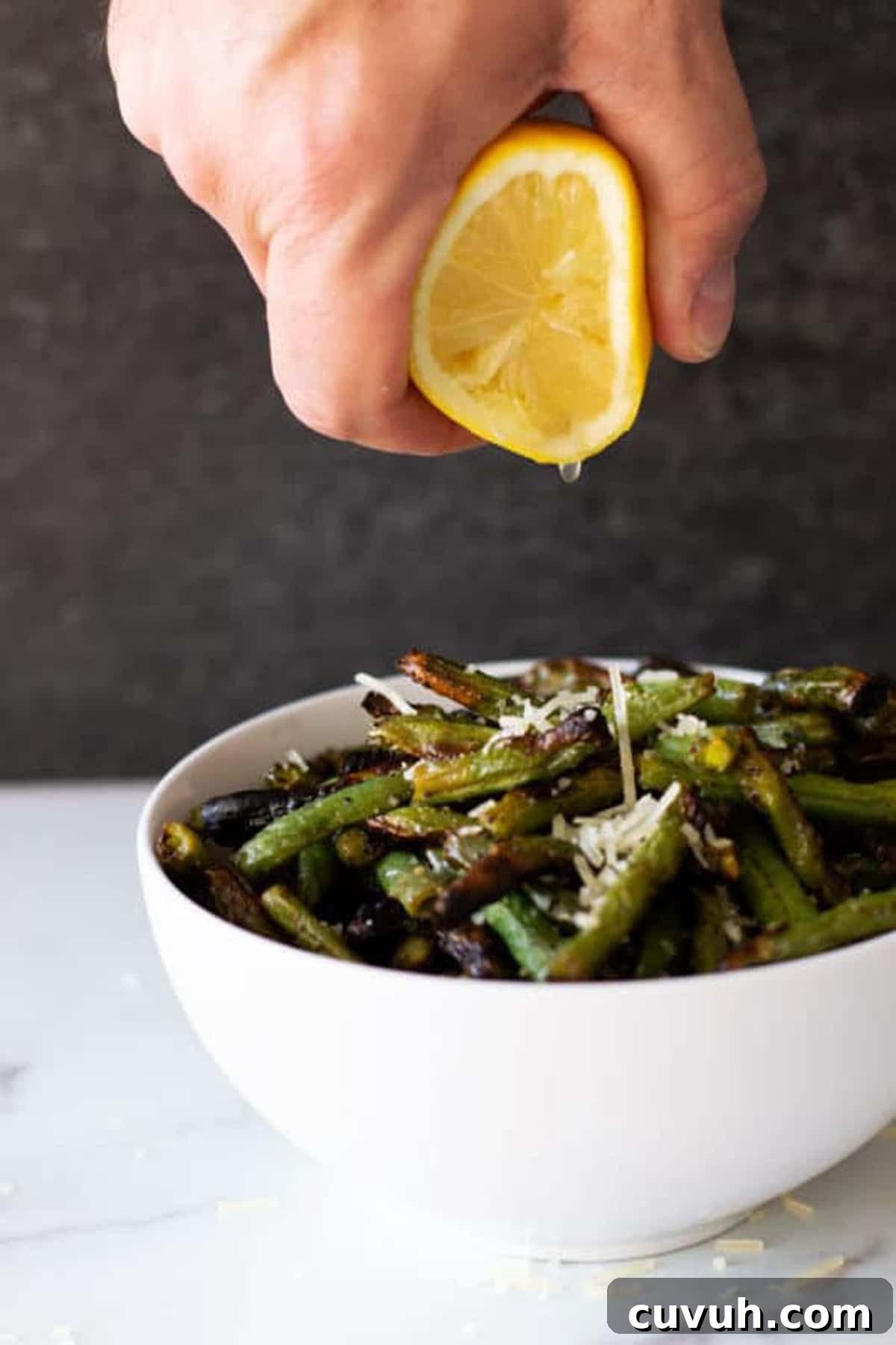 Person squeezing lemon juice on fresh grilled green beans. 