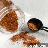 Taco seasoning spilling from a mason jar with a tablespoon on the side filled with taco seasoning.