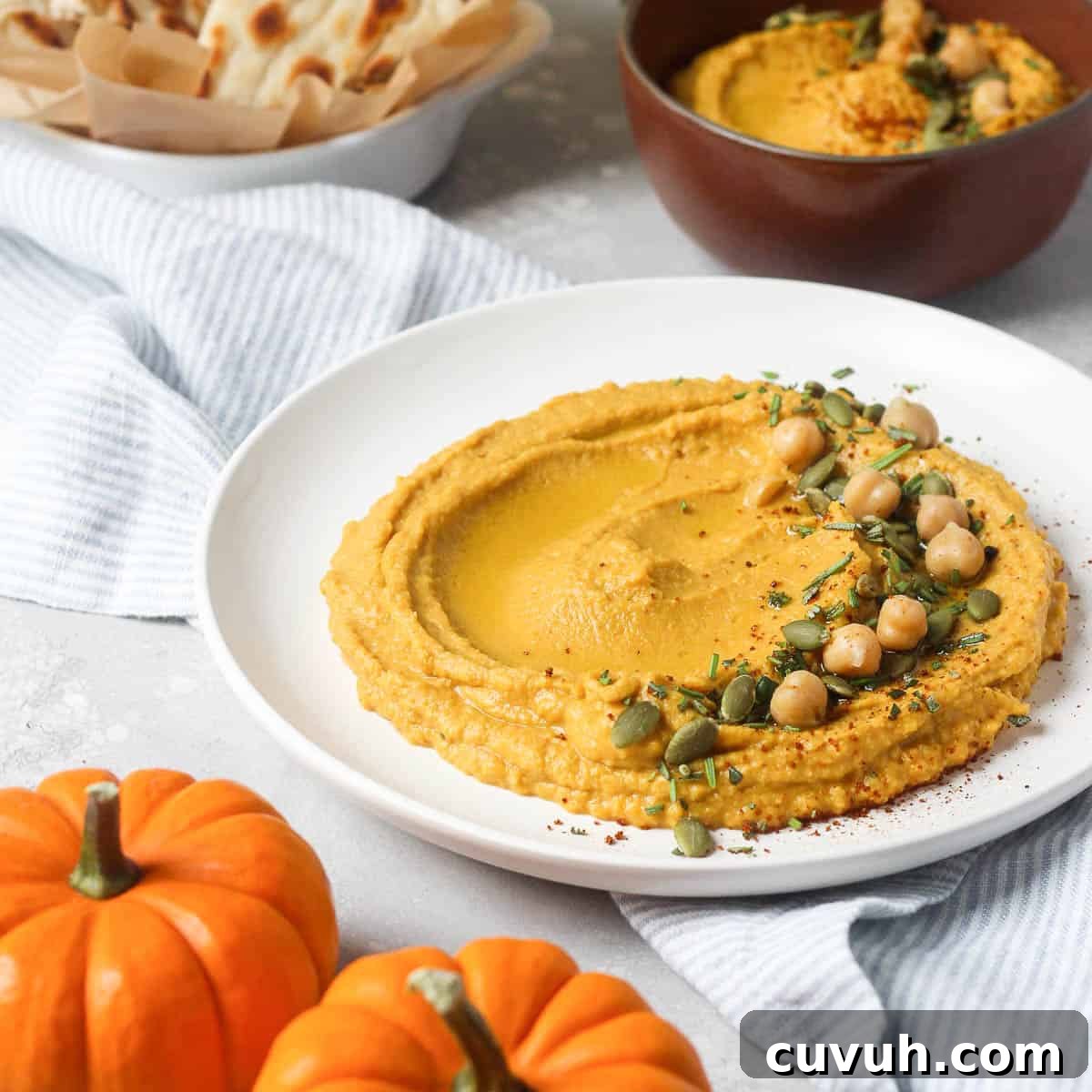 Thanksgiving Appetizers You Can Make Ahead for Stress-Free Hosting 3 Pumpkin hummus on white plate with chick peas.