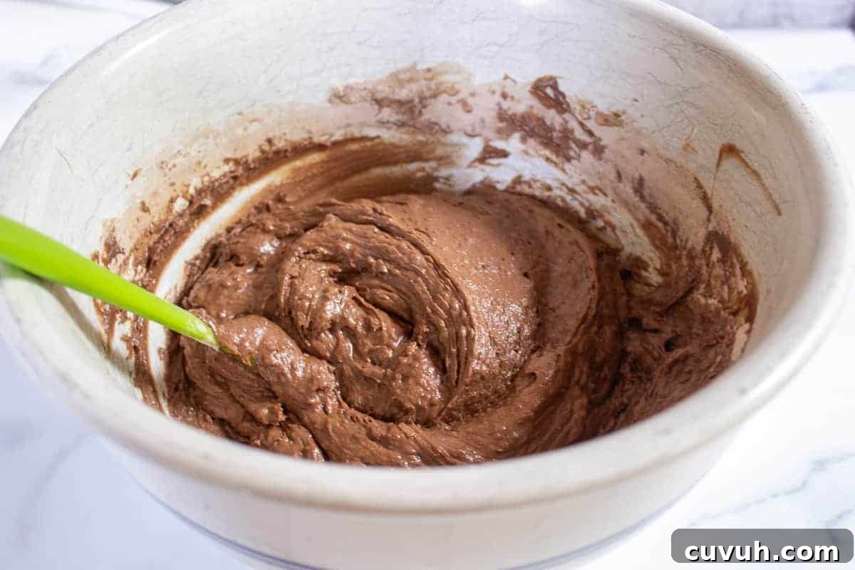 Chocolate muffin batter in a large bowl with a green spatula.